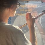 London Sign Writer, Seraina Baumgartner is a contemporary Swiss graphic designer and letterform artist known for her refined use of classical Roman lettering traditions within modern design contexts. Her work frequently draws on historical serif typefaces such as Caslon, Baskerville, and Trajan, using their proportions and structural logic as a foundation rather than treating them as decorative pastiche. Baumgartner’s approach reflects a kinship understanding of inscriptional Roman capitals and early print book typography. Typefaces like Caslon and Baskerville populate her work through their balance of calligraphic stroke contrast and elegant forms, while Trajan’s influence is evident in her use of monumental capitals, classical spacing, and stone-carved strength. Her design agility references her work with a sense of classicism, authority, and legibility. The core qualities closely associated with Roman letterforms and her Italian/Swiss origins. What distinguishes Baumgartner’s use of these styles is her restraint and controlled scaling. Rather than falling into the common trap of many young graphic designers of overt overdressed graphic historicism. Seraina retains their essential principles — proportion, rhythm, and spacing hierarchy — and applies them to contemporary commercial worlds of retail layouts, wayfinding, and private house titles and numerals. This aligns her own heritage and design practice with a humanist modernist tradition, embracing classical Roman typography via the lens of Swiss graphic design precision.