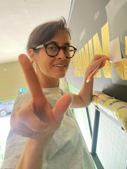 Seraina Baumgartner is a contemporary Swiss graphic designer and letterform artist known for her refined use of classical Roman lettering traditions within modern design contexts. Her work frequently draws on historical serif typefaces such as Caslon, Baskerville, and Trajan, using their proportions and structural logic as a foundation rather than treating them as decorative pastiche. Baumgartner’s approach reflects a kinship understanding of inscriptional Roman capitals and early print book typography. Typefaces like Caslon and Baskerville populate her work through their balance of calligraphic stroke contrast and elegant forms, while Trajan’s influence is evident in her use of monumental capitals, classical spacing, and stone-carved strength. Her design agility references her work with a sense of classicism, authority, and legibility. The core qualities closely associated with Roman letterforms and her Italian/Swiss origins. What distinguishes Baumgartner’s use of these styles is her restraint and controlled scaling. Rather than falling into the common trap of many young graphic designers of overt overdressed graphic historicism. Seraina retains their essential principles — proportion, rhythm, and spacing hierarchy — and applies them to contemporary commercial worlds of retail layouts, wayfinding, and private house titles and numerals. This aligns her own heritage and design practice with a humanist modernist tradition, embracing classical Roman typography via the lens of Swiss graphic design precision.