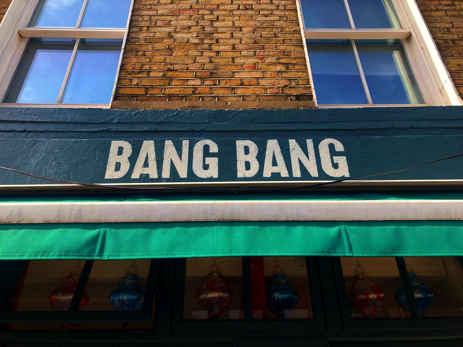 Storefront with a bold white 'BANG BANG' sign above a teal awning on a brick building.