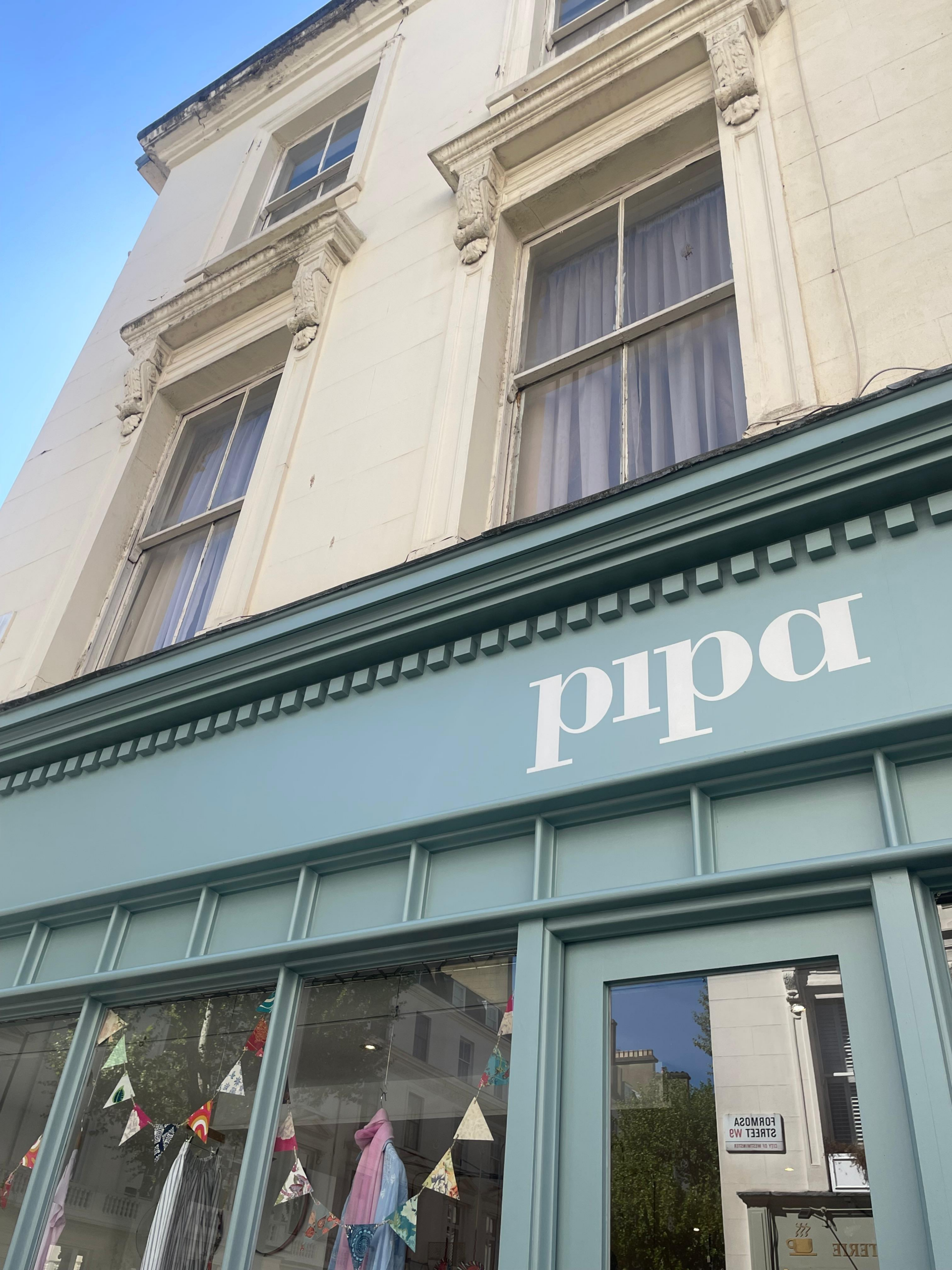 Storefront window with red frame and brick building, displaying colorful paper roses in the window and a gold Pipa sign above.