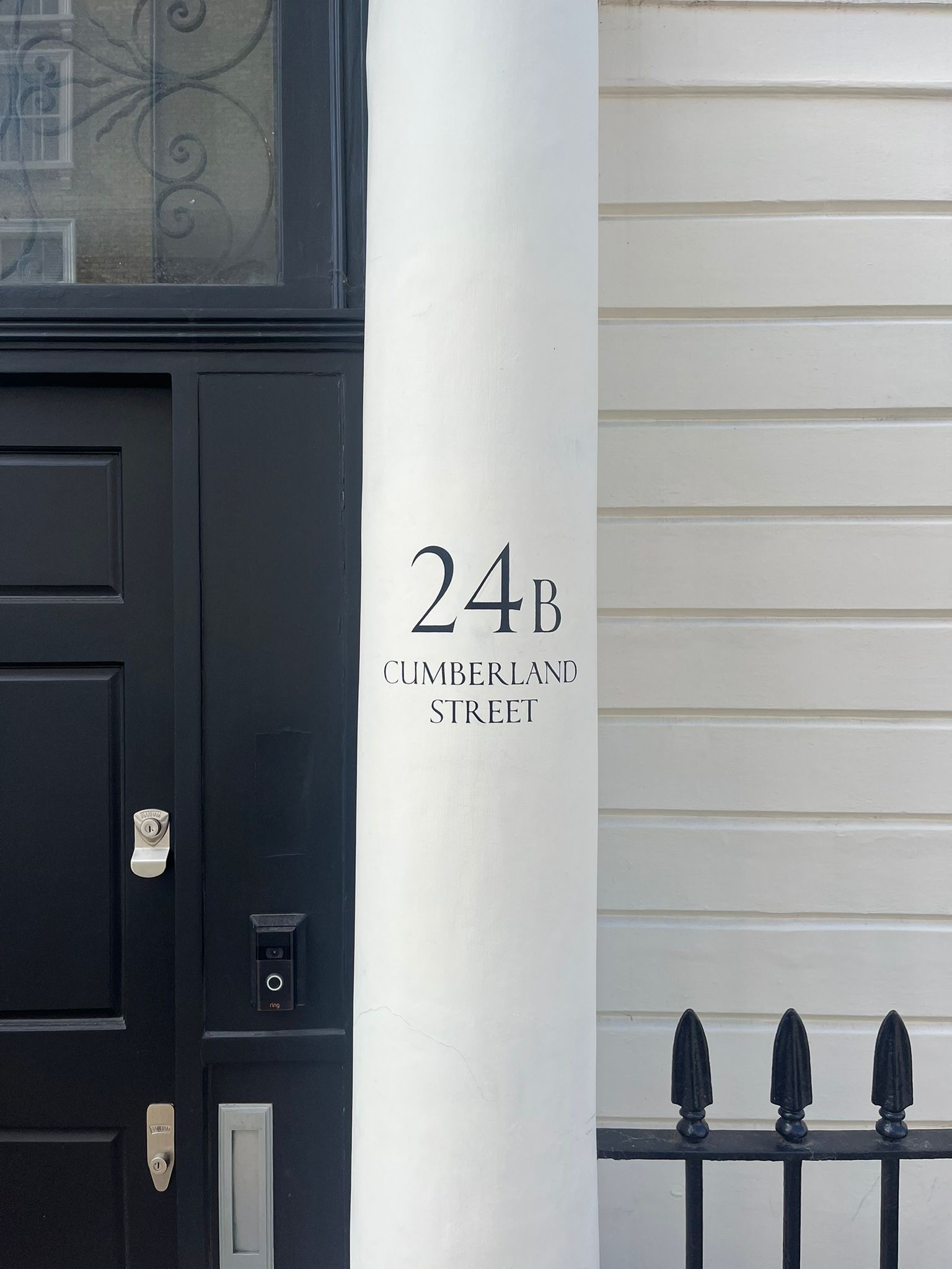 White column with the text 24B Cumberland Street beside a dark front door and pale siding; a small wrought-iron fence is visible on the right. White column with the text 24B Cumberland Street beside a dark front door and pale siding; a small wrought-iron fence is visible on the right.